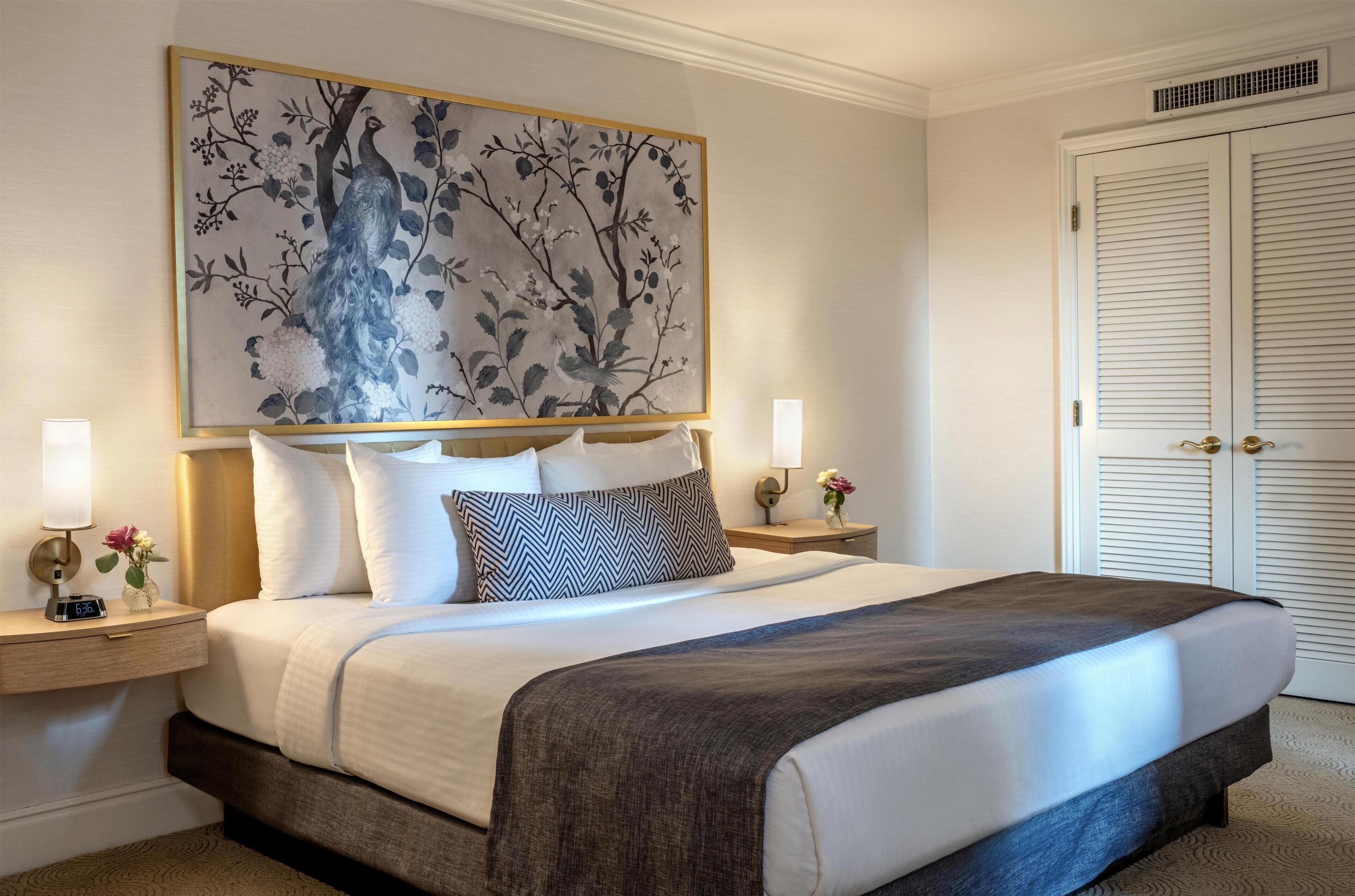 A hotel room with a large bed, two bedside tables with lamps, a wall-mounted artwork, and a door with a window.