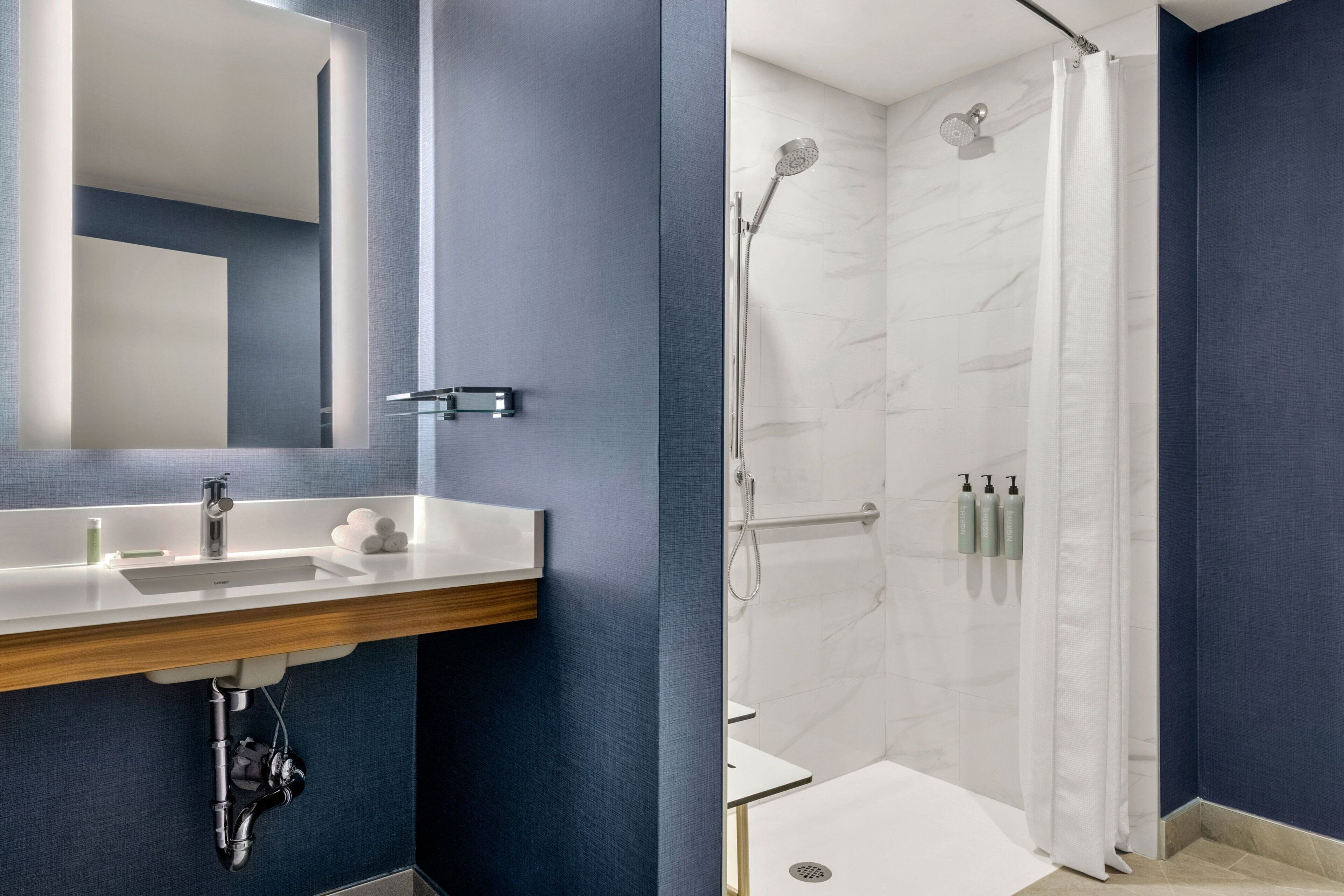 A modern bathroom with a large mirror, a sink, and a shower area.