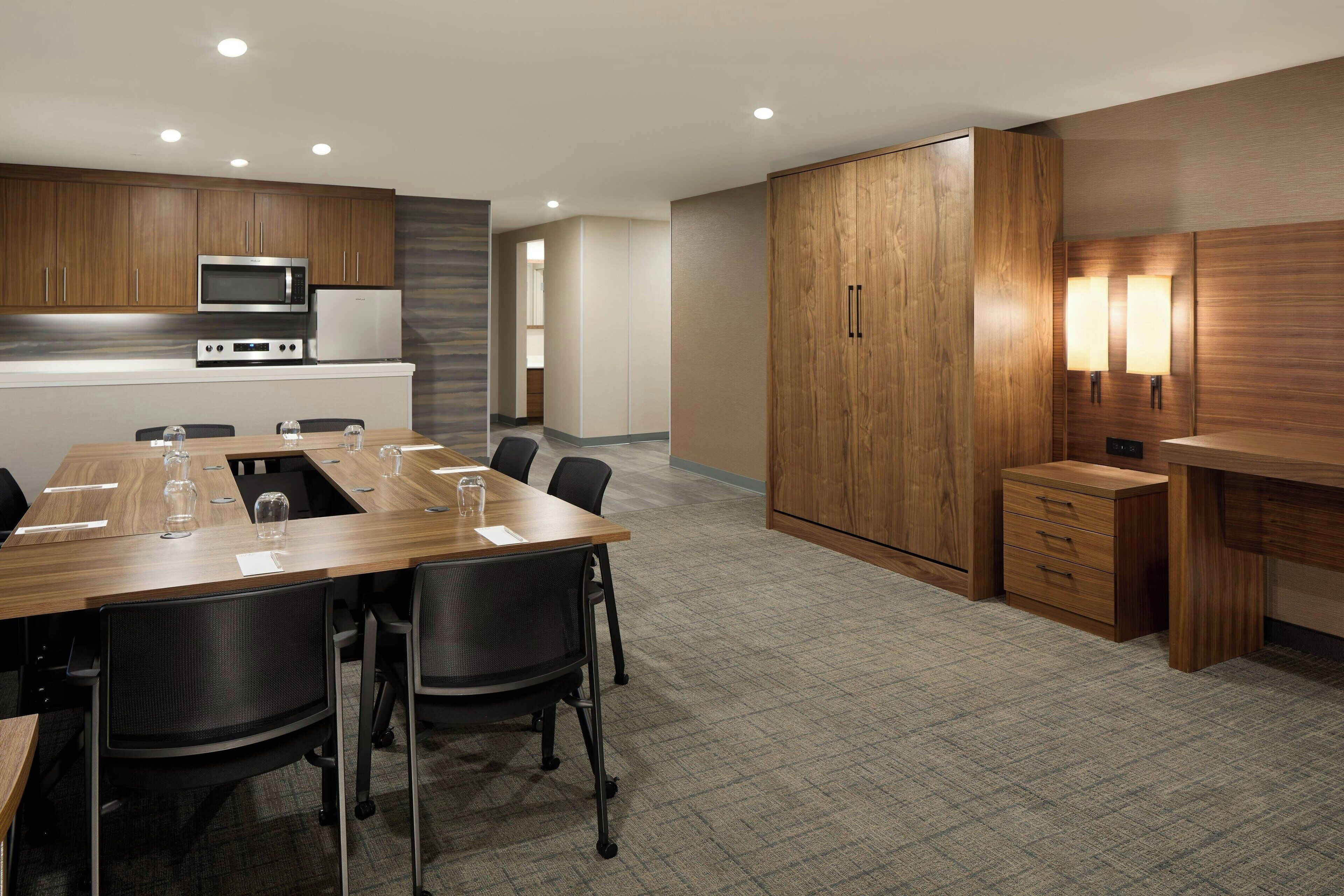 A modern kitchen with built-in appliances, a dining area with a long table and chairs, and a wooden wardrobe.