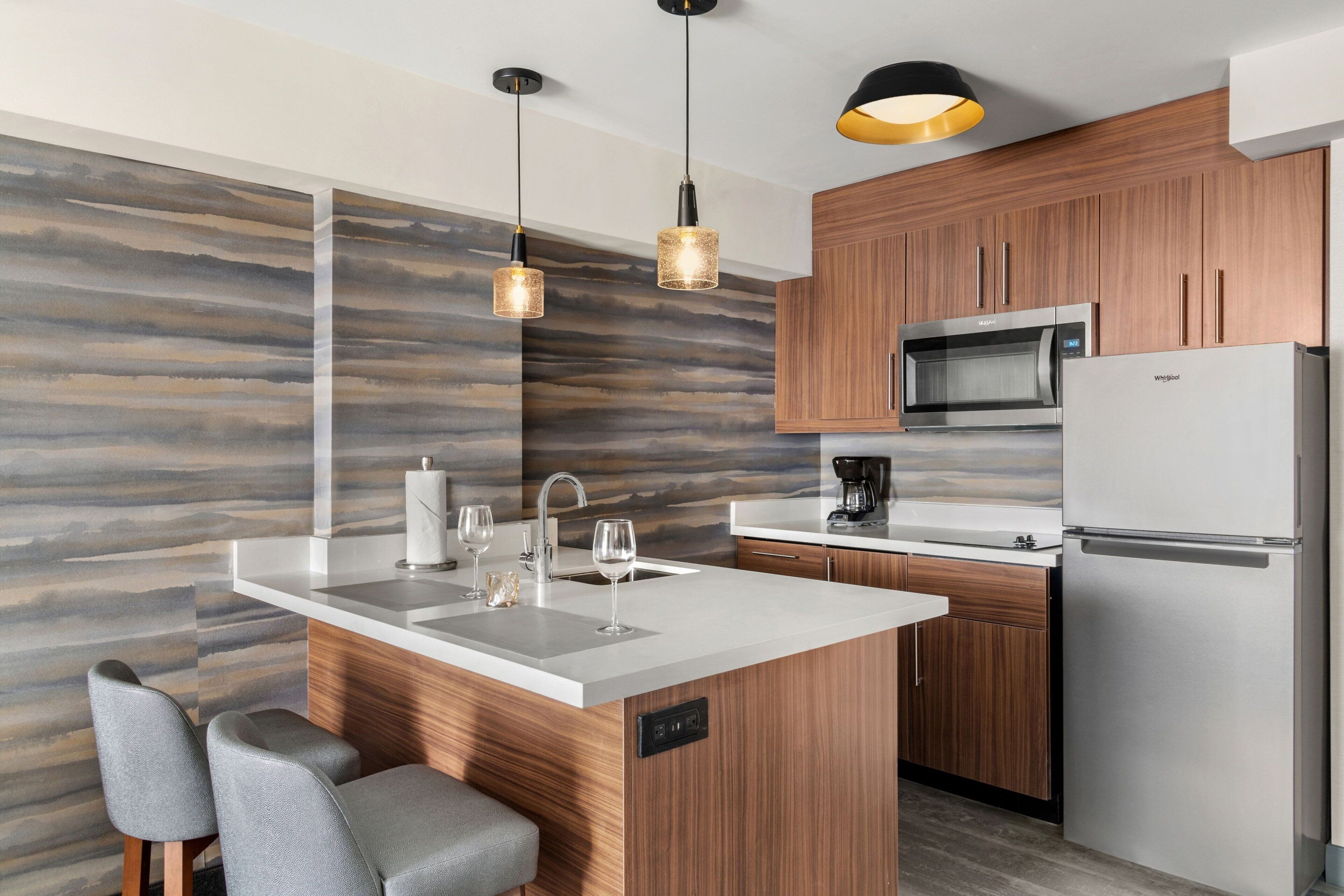 A modern kitchen with wooden cabinets, stainless steel appliances, a central island with seating, and pendant lighting.