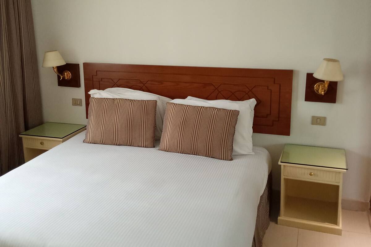 A hotel room with a large bed, two bedside tables, and two wall-mounted lamps.