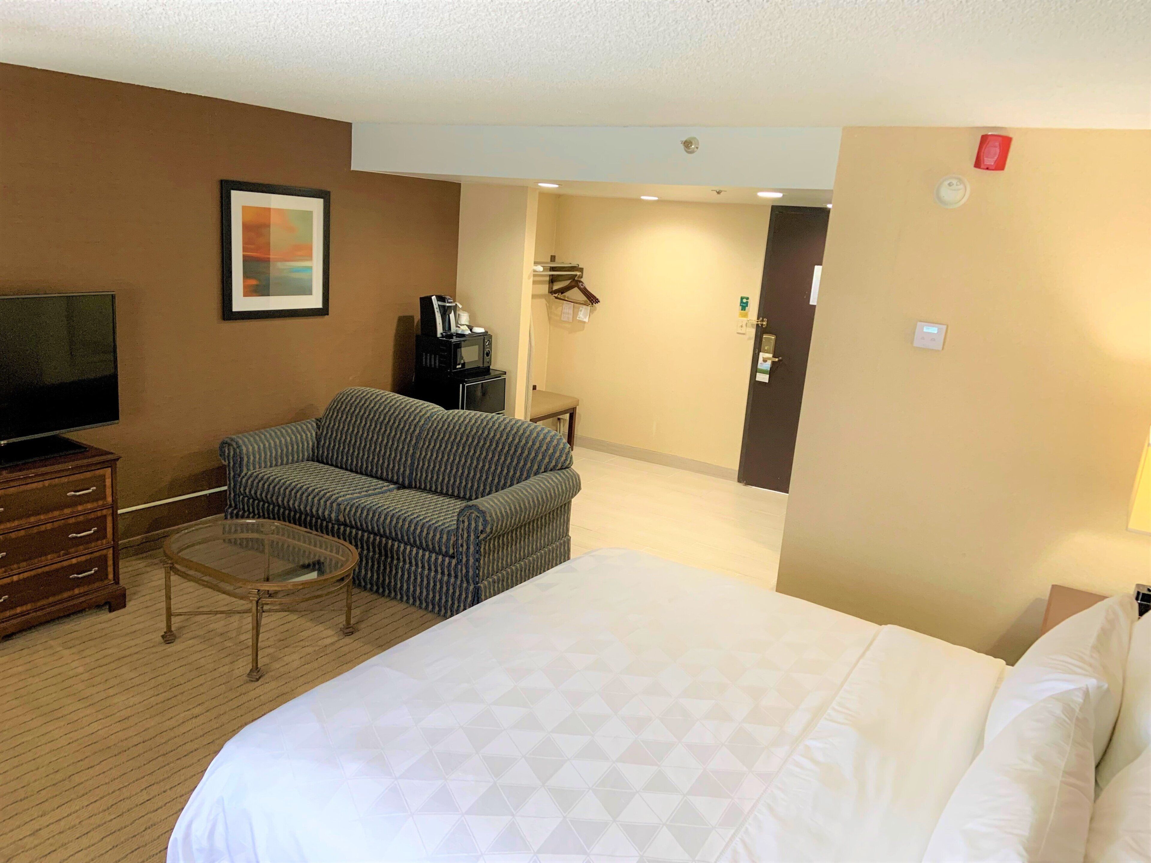 A hotel room with a large bed, a sofa, a television, a coffee maker, and a framed picture on the wall.