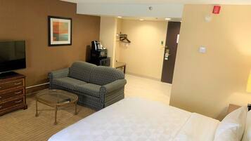 A hotel room with a large bed, a sofa, a television, a coffee maker, and a framed picture on the wall.