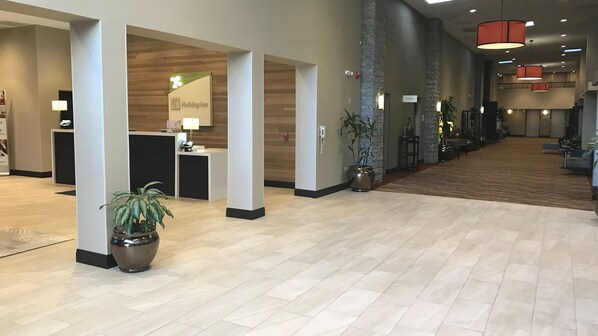 A hotel lobby with a reception desk, potted plants, and a carpeted floor.