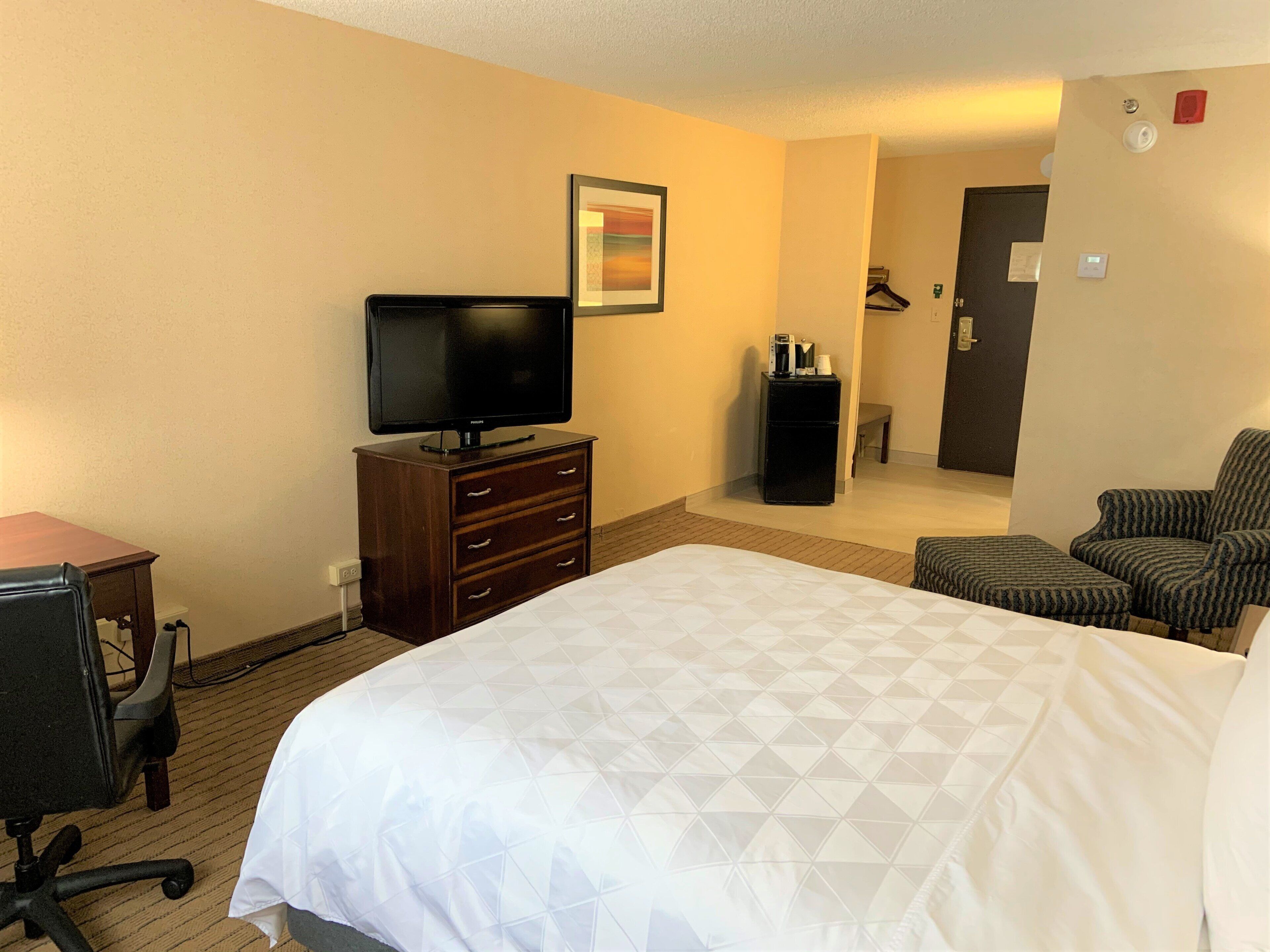 Quarto de hotel com cama, televisão, escrivaninha e uma cadeira.