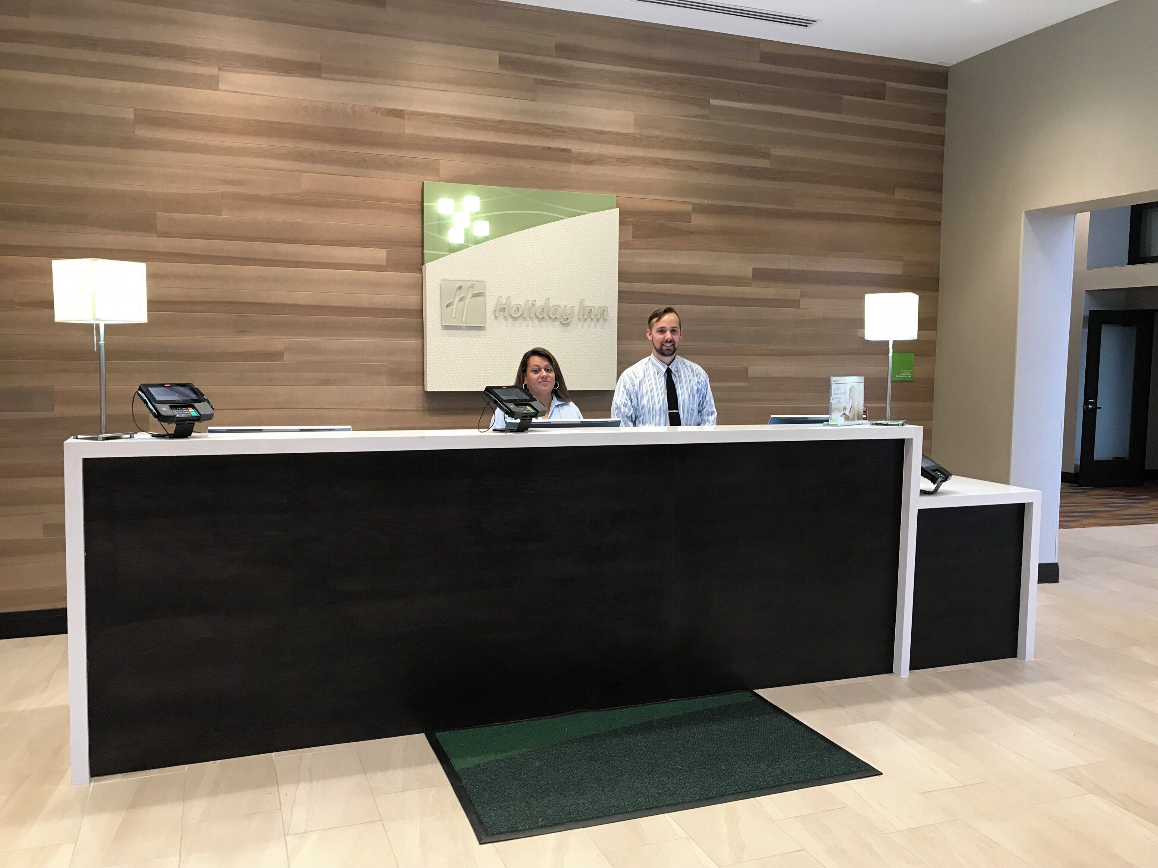A reception desk with a logo, a man and a woman behind it, and a lamp on each side.