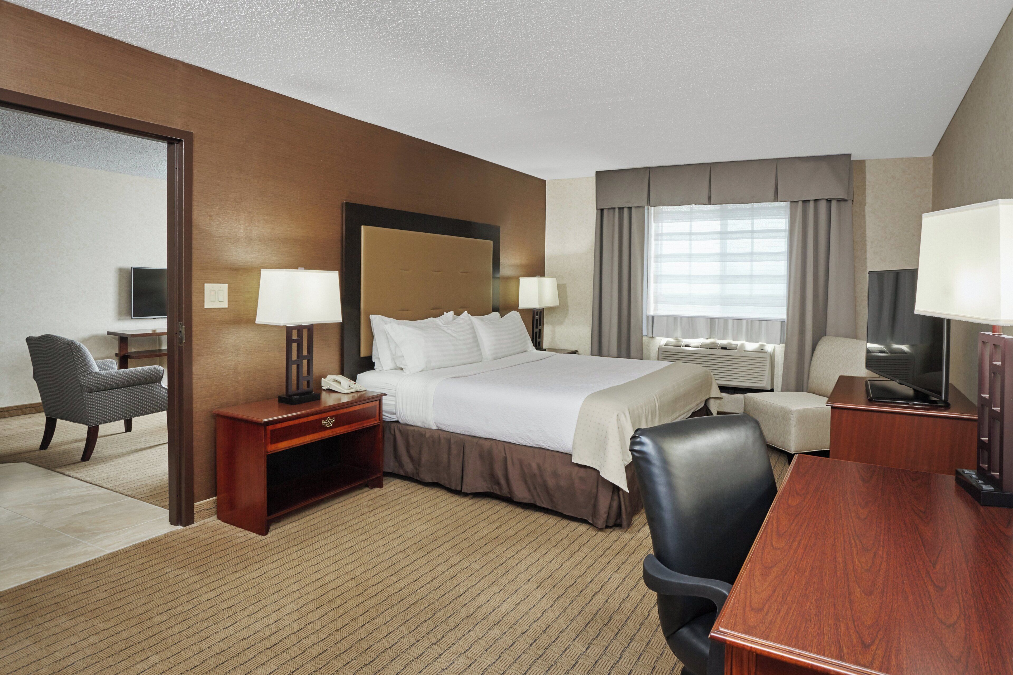 A hotel room with a bed, bedside tables, a desk, a chair, a television, and a window with curtains.