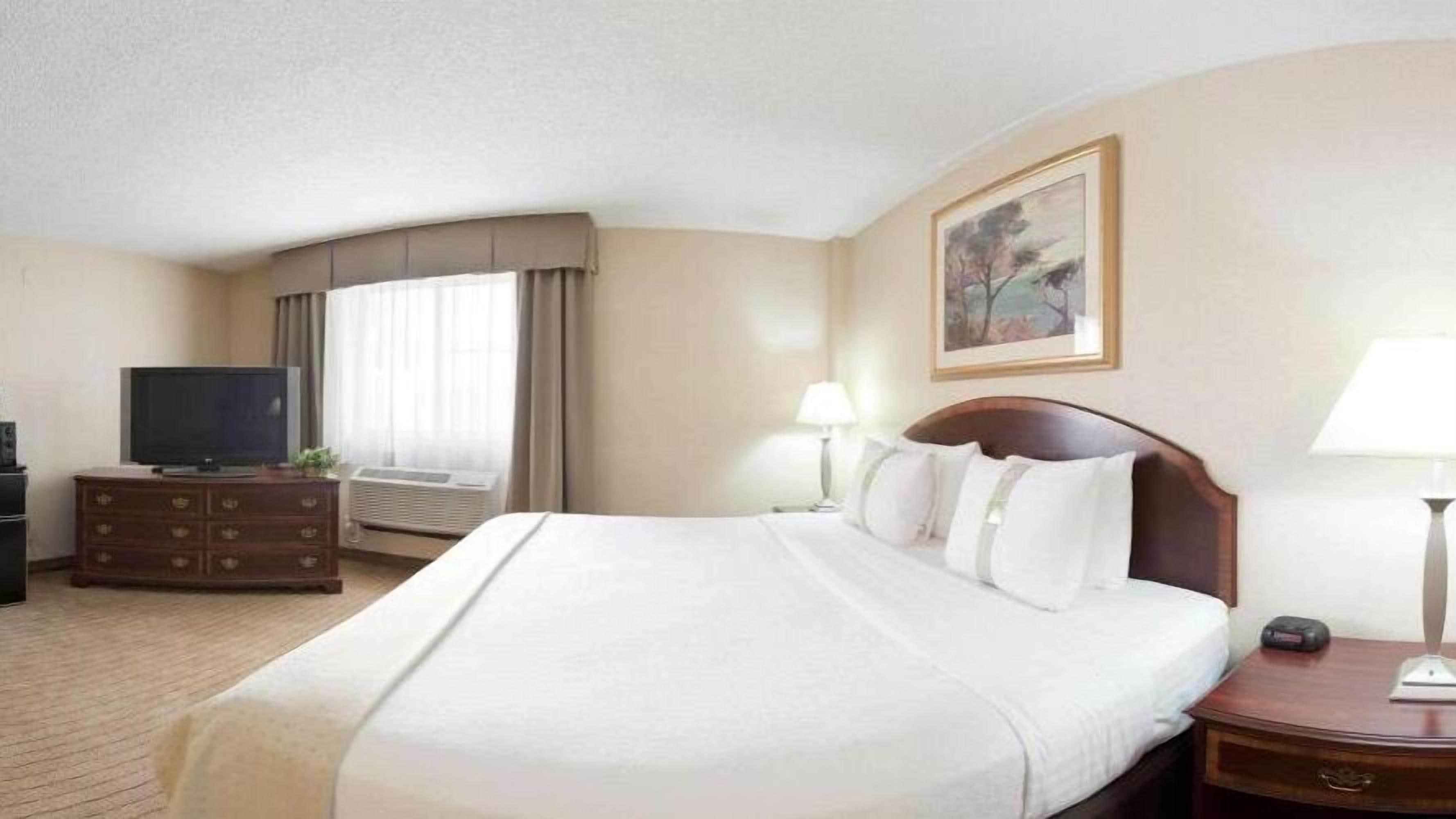 A hotel room with a large bed, a TV, a dresser, and a window with curtains.