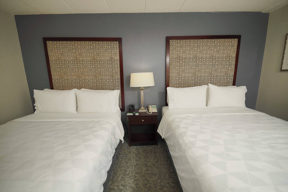 A hotel room with two beds, a nightstand with a lamp, and a patterned headboard.