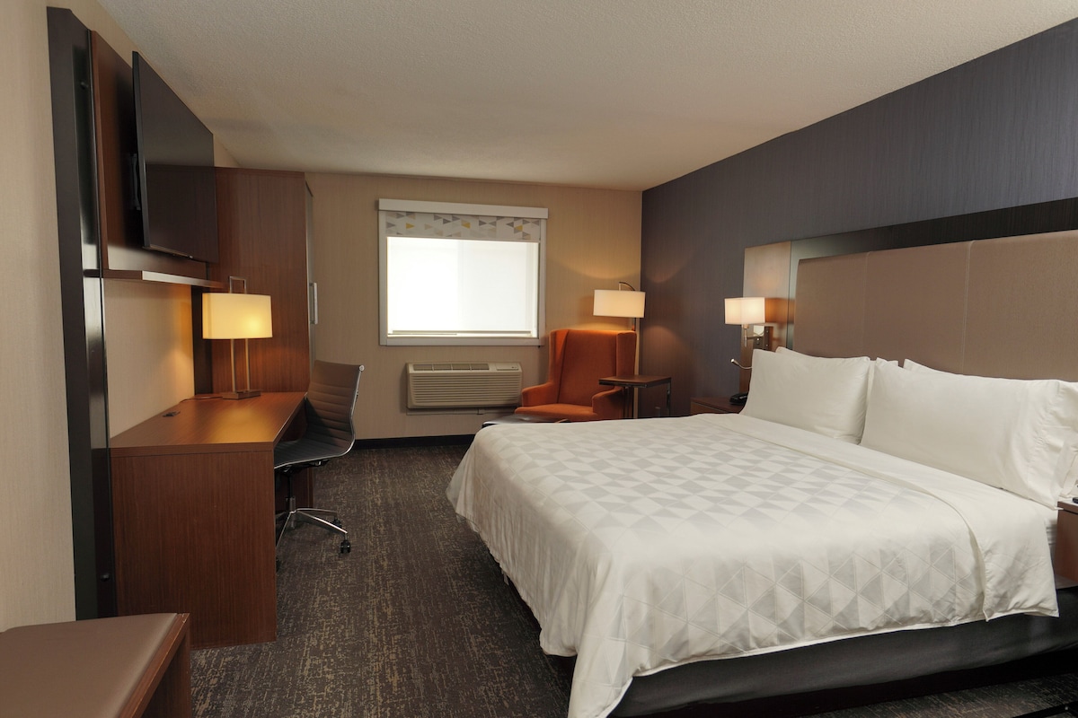 Een hotelkamer met een bed, bureau, stoel, televisie en lampen.