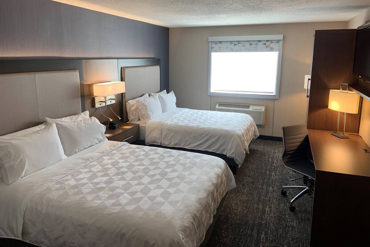 A hotel room with two beds, a desk, a chair, and a window.