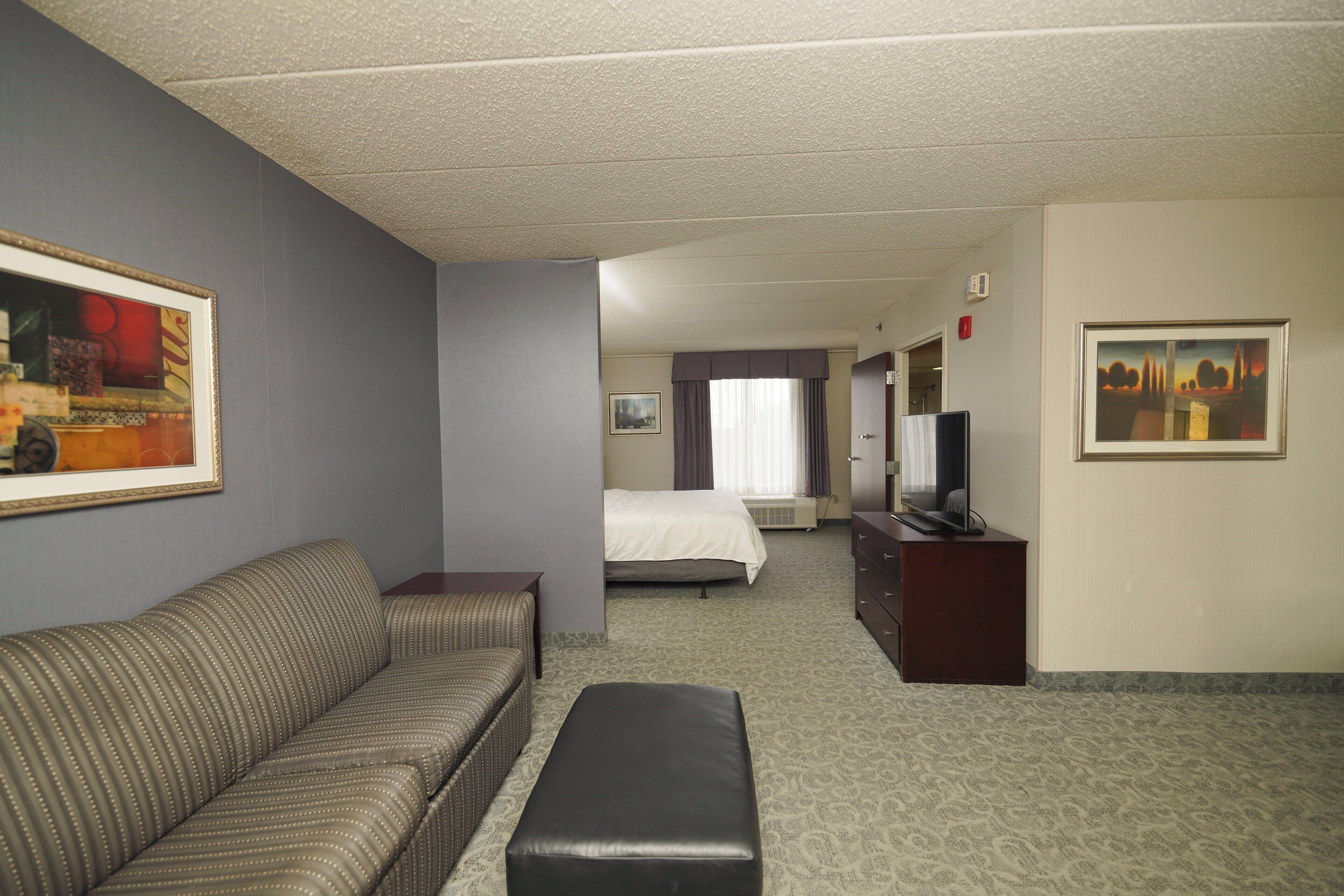 A hotel room with a sofa, a small table, a bed, a television, and artwork on the walls.