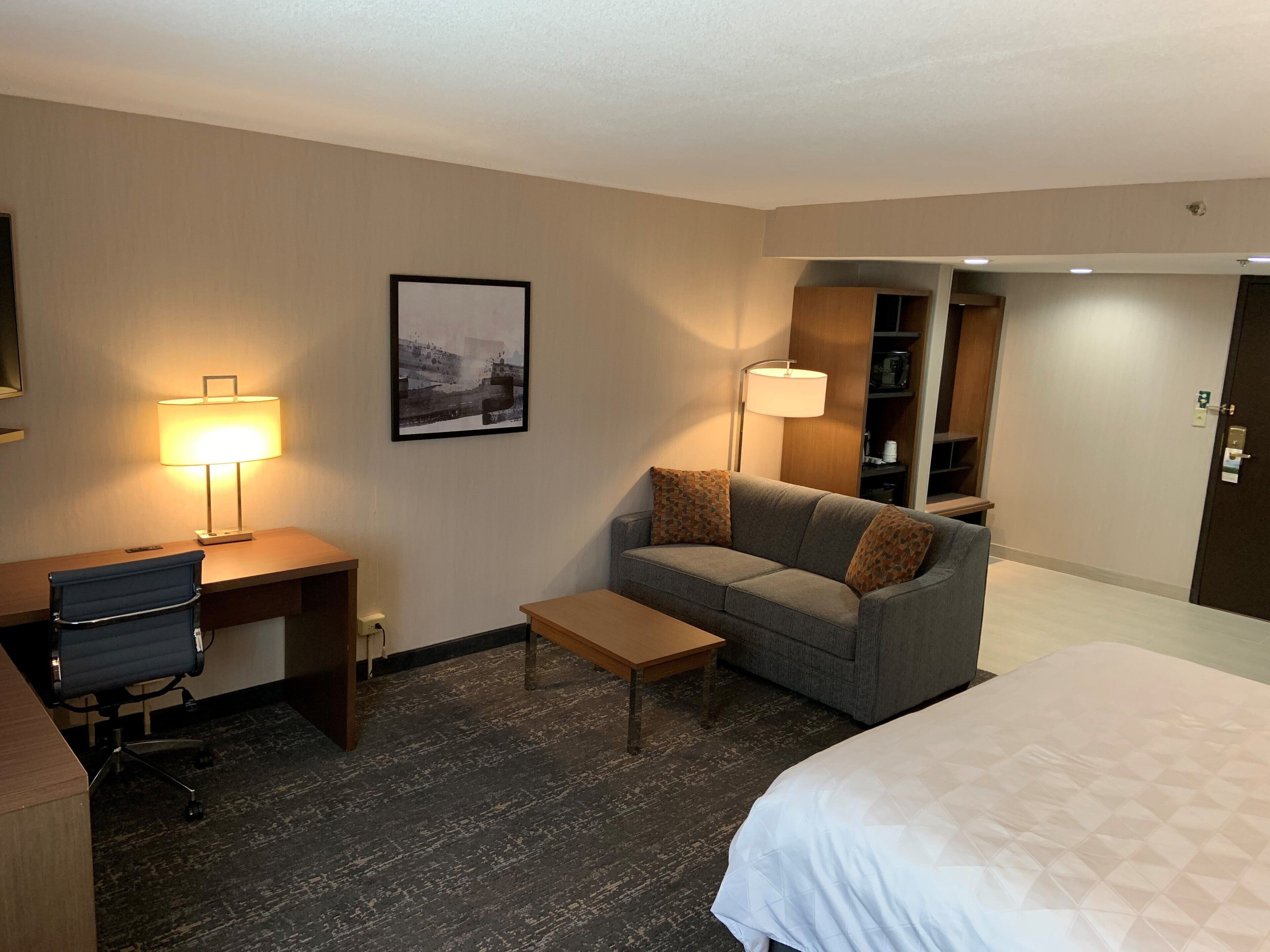 Une chambre d’hôtel comprenant un lit, un bureau avec une chaise, un canapé, une table basse et une lampe.