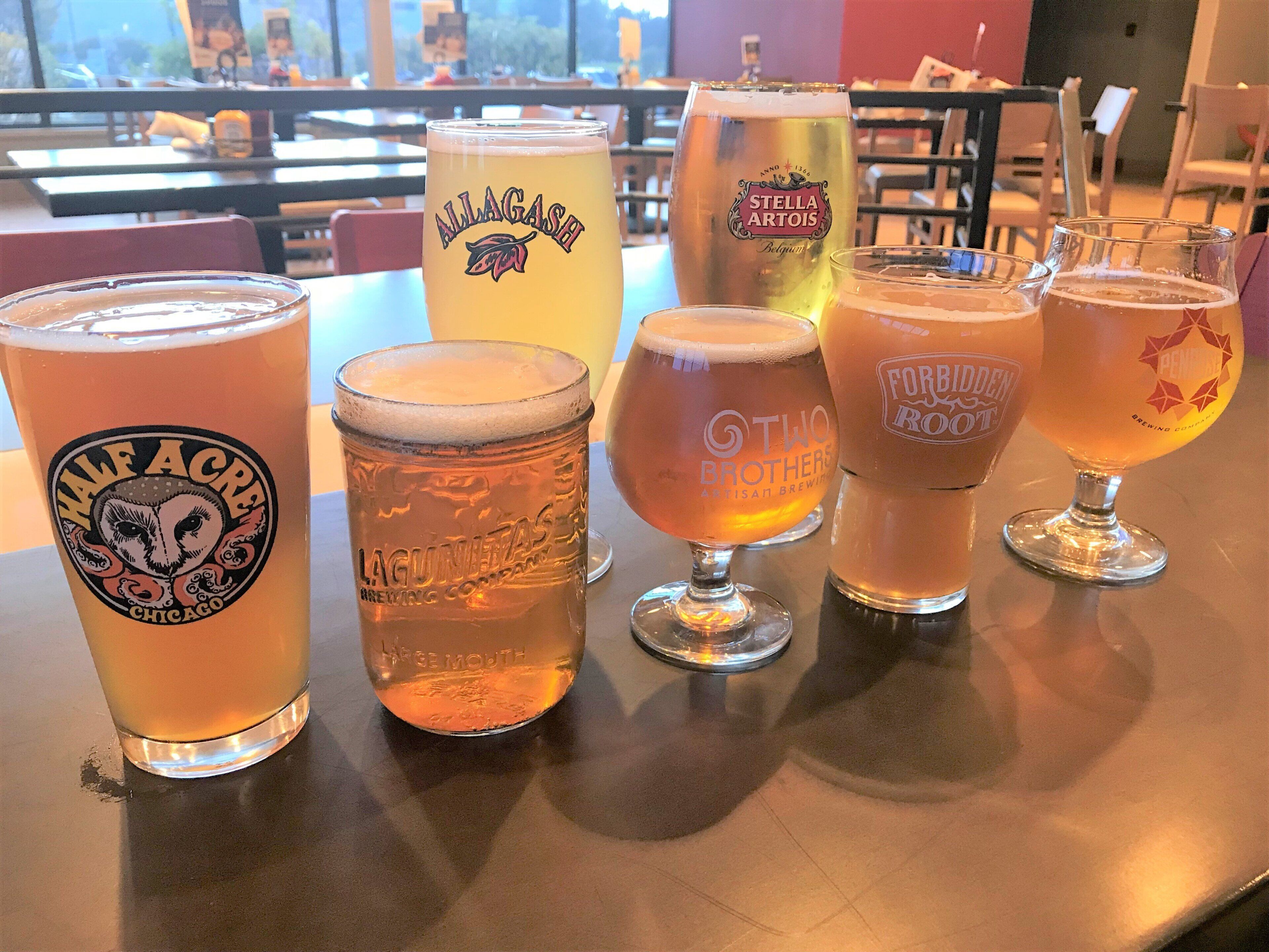 Verschiedene Biergläser auf einem Tisch, verziert mit unterschiedlichen Brauereietiketten.