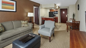 A living room with a sofa, ottoman, armchair, and a dining table with chairs. - Holiday Inn & Suites Chicago-Carol Stream (Wheaton) by IHG (Carol Stream)