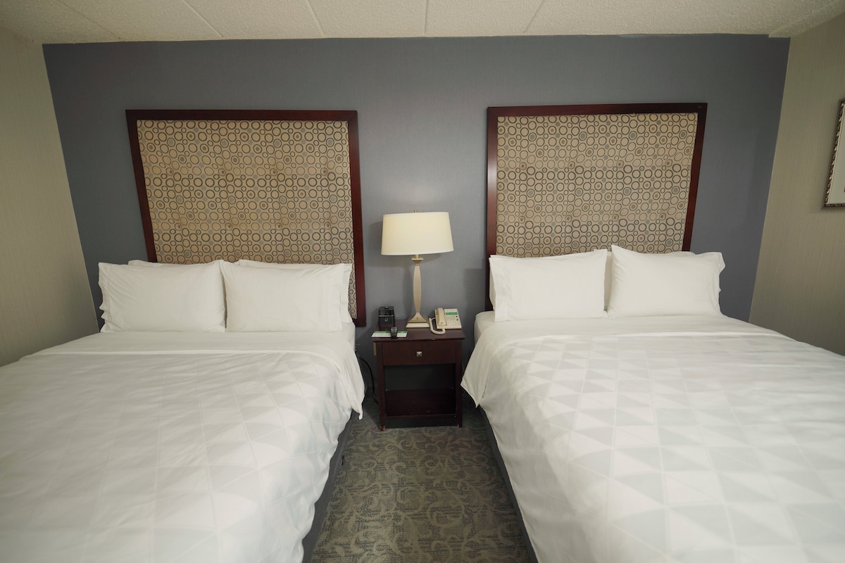 Een hotelkamer met twee bedden, een nachtkastje met een lamp en een gestreept hoofdeinde.