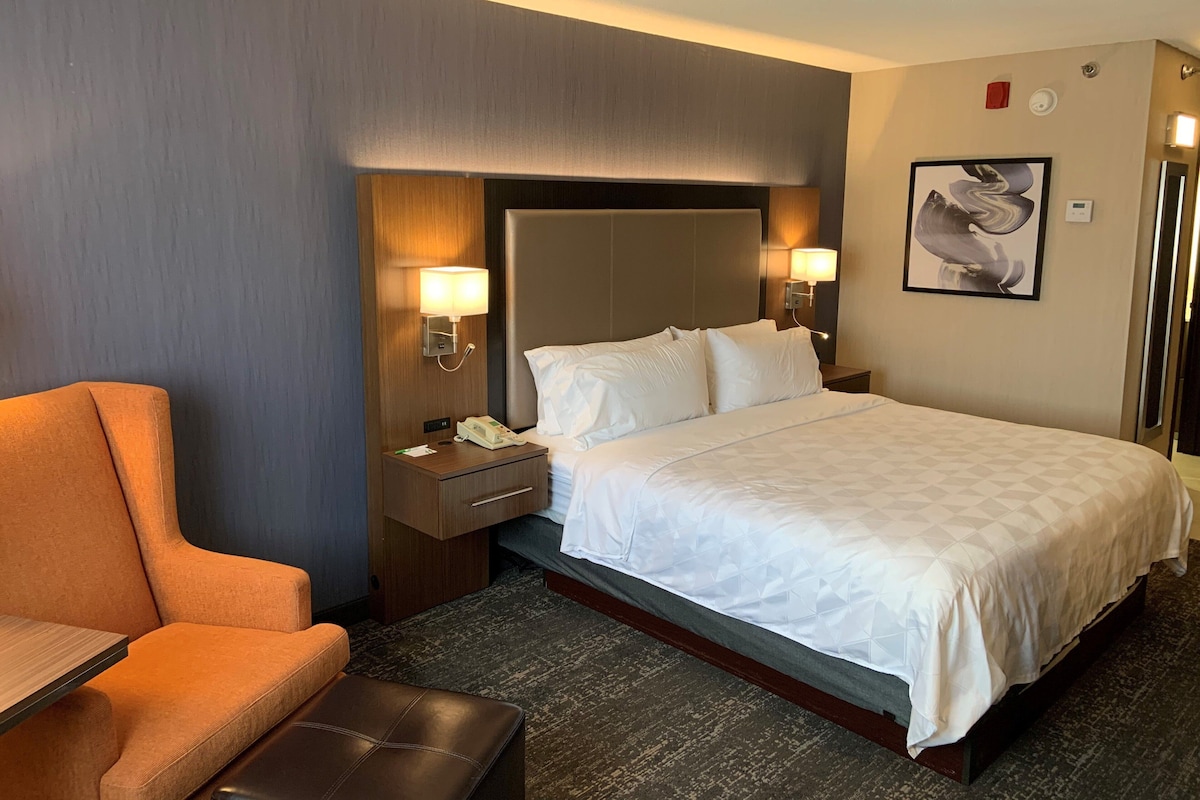 Een hotelkamer met een bed, nachtkastje, telefoon, stoel en een wandlamp.