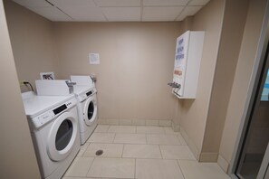 Een wasserette met twee voorladers, een droger en een zeepdispenser aan de muur.
