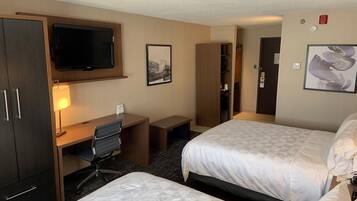A hotel room with two beds, a desk with a chair, a television mounted on the wall, and a door leading to a closet.