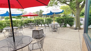An outdoor patio with round tables and chairs, red and white umbrellas, and a fire pit. - Holiday Inn & Suites Chicago-Carol Stream (Wheaton) by IHG (Carol Stream)