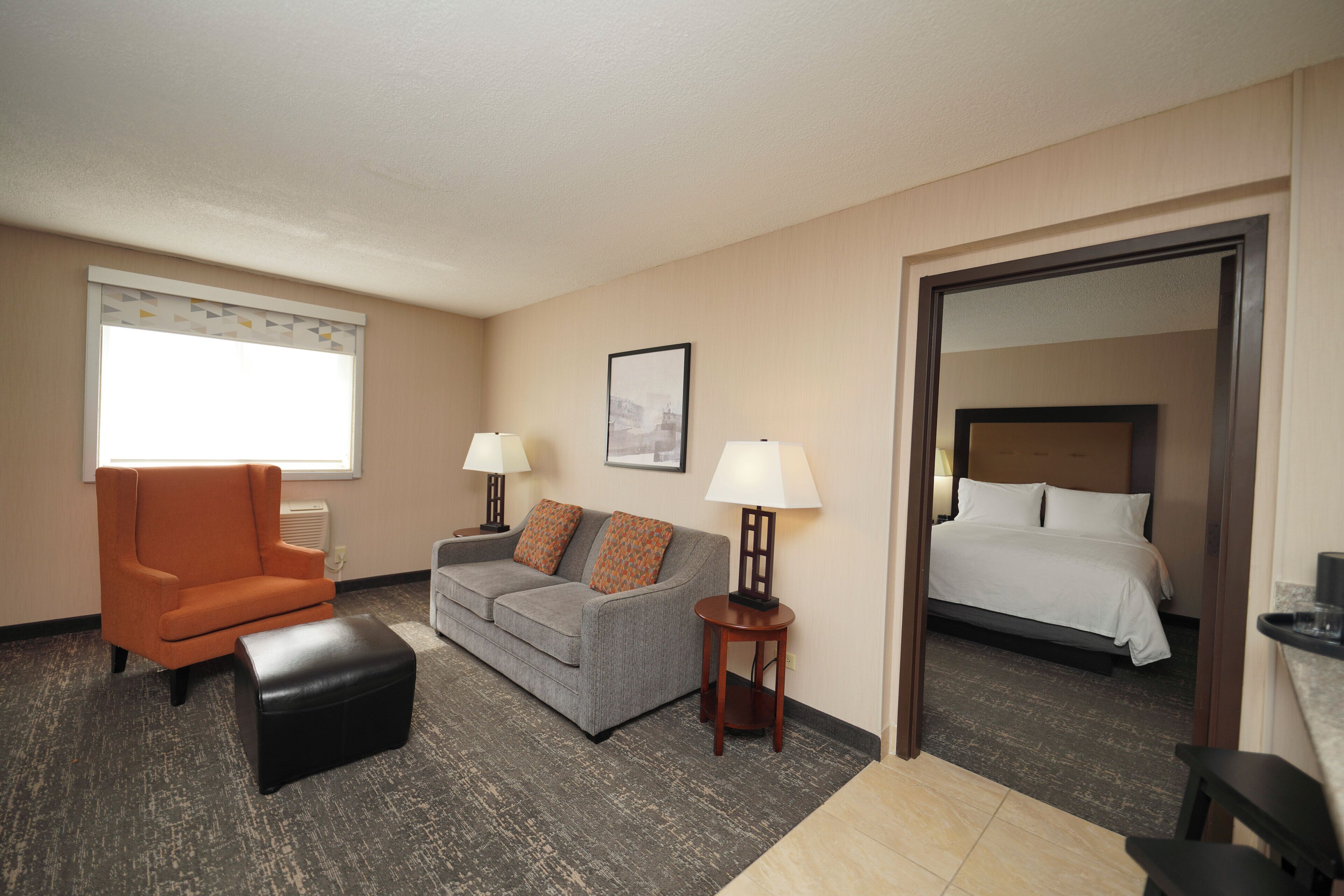 A hotel room with a sofa, armchair, and a bed. There are two lamps on the floor.