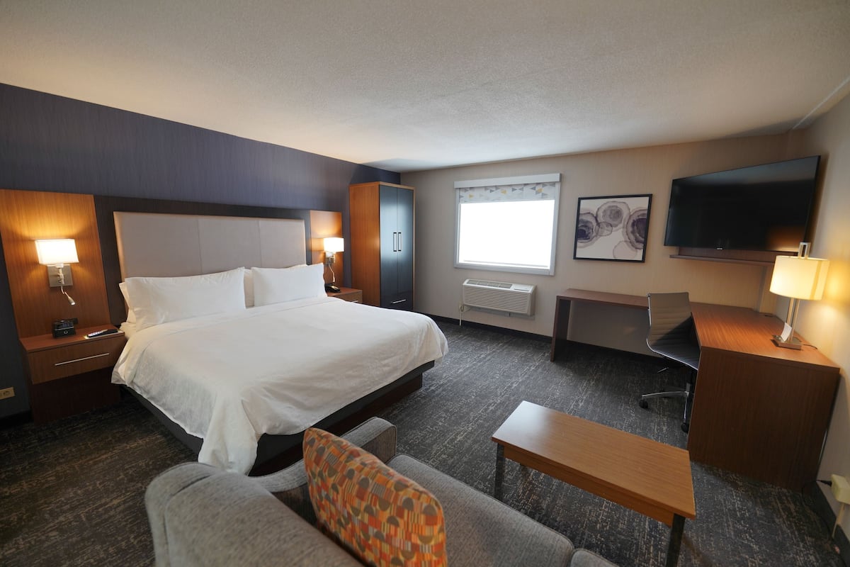 A hotel room with a large bed, a desk, a chair, a TV, and a window with curtains.