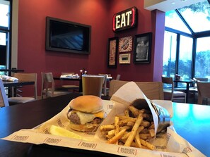 A restaurant interior with a burger and fries on a table, framed pictures on the wall, and a 'EAT' sign.