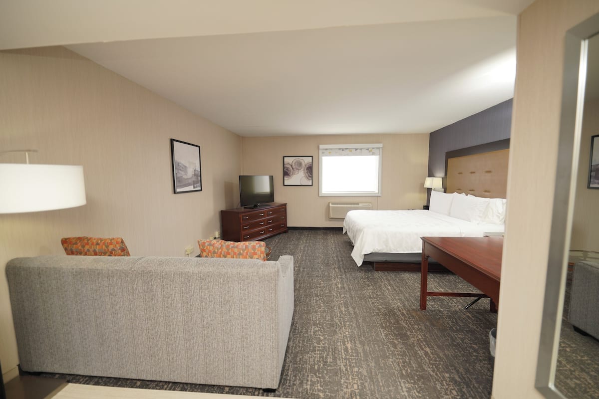 A hotel room with a bed, a sofa, a TV, a dresser, and a window.
