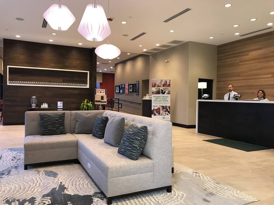 A modern hotel lobby with a sectional sofa, a reception desk, and a dining area.