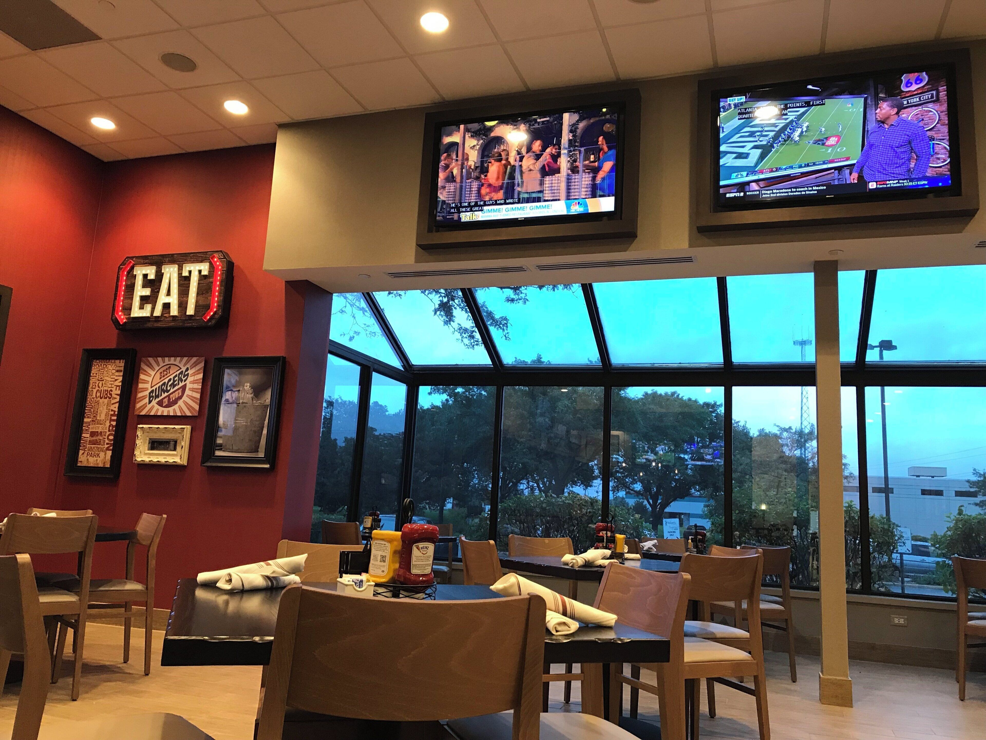 A restaurant interior with multiple tables, chairs, and a large window offering a view of the outdoors.
