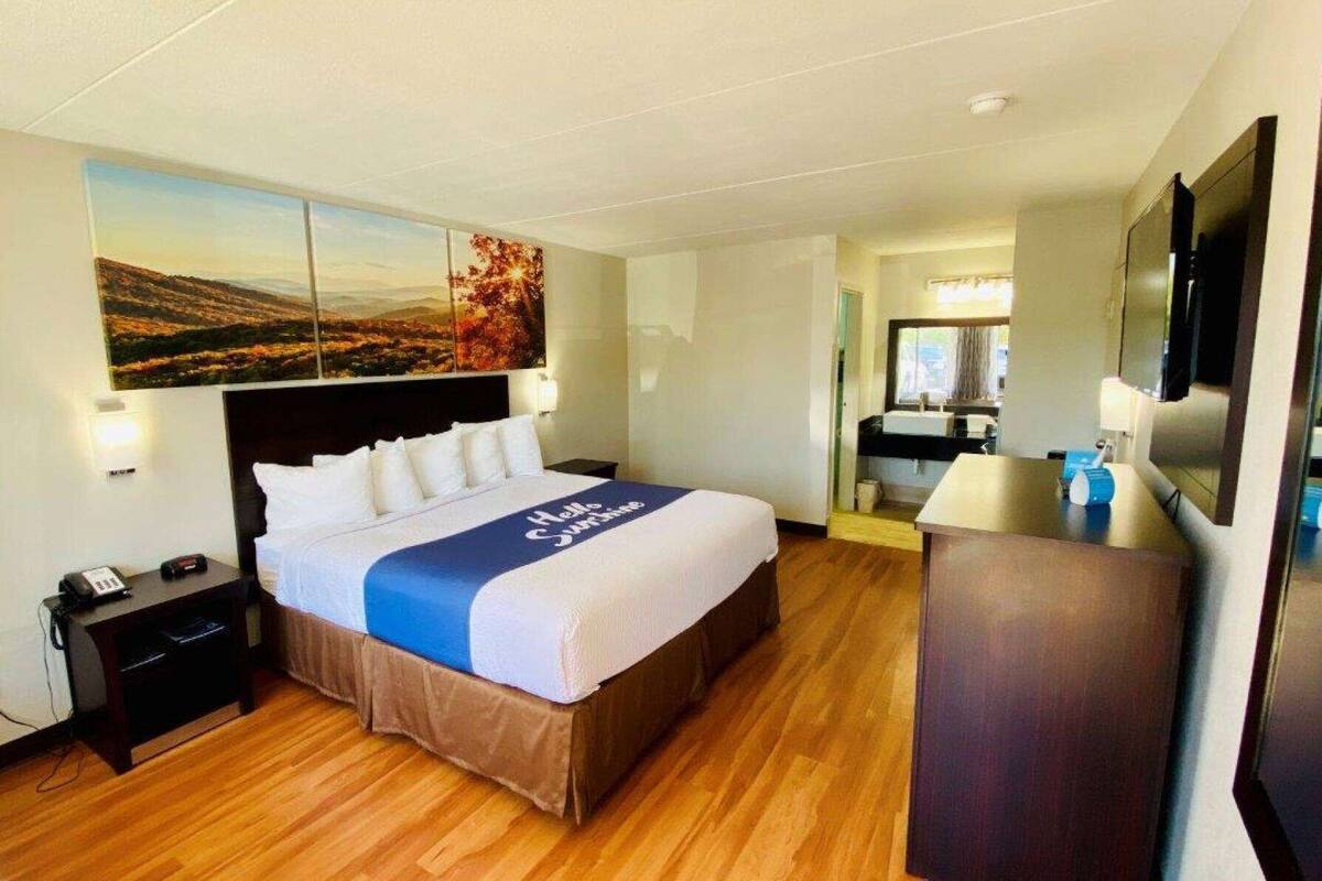 A hotel room with a bed, a desk, a mirror, and a TV.