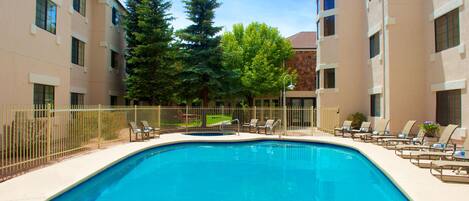 A swimming pool with lounge chairs and a fence, surrounded by trees and buildings.