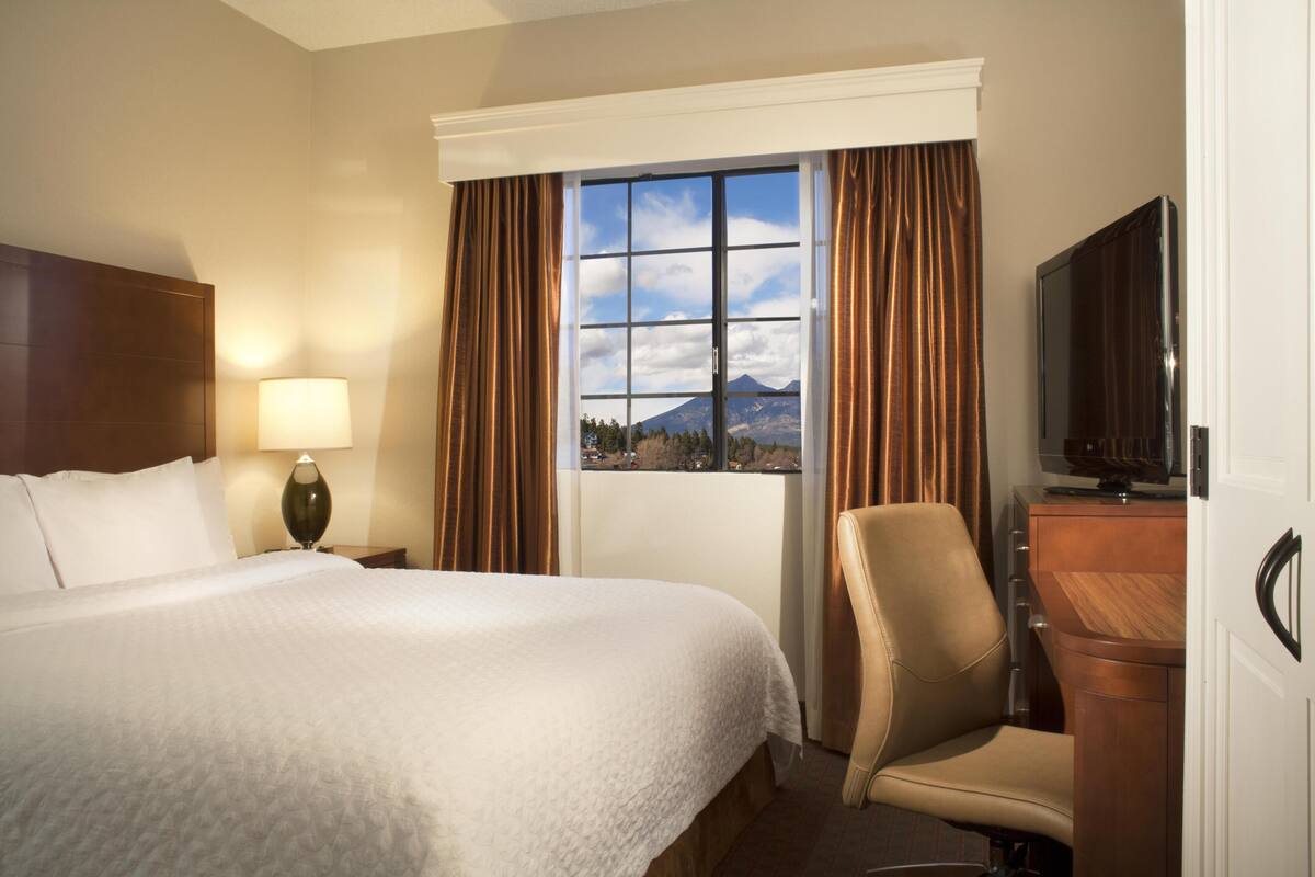 Ein Hotelzimmer mit Bett, Schreibtisch, Stuhl, Fernseher und Fenster mit Bergblick.