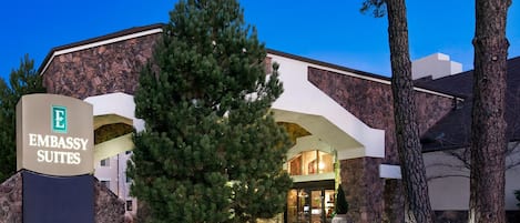 A building with a sign for Embassy Suites, featuring a modern architectural style with a prominent entrance and surrounding trees.