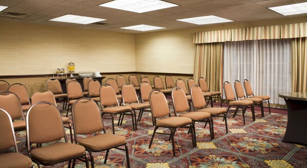 Un salón de conferencias con filas de sillas, una mesa y una alfombra estampada.
