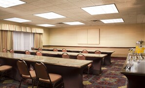 A conference room with a long table, chairs, a projector screen, and a coffee station.