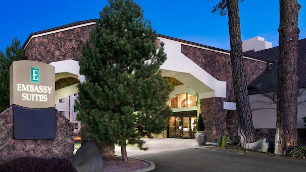 A building with a sign for Embassy Suites, featuring a modern architectural style with a prominent entrance and surrounding trees.