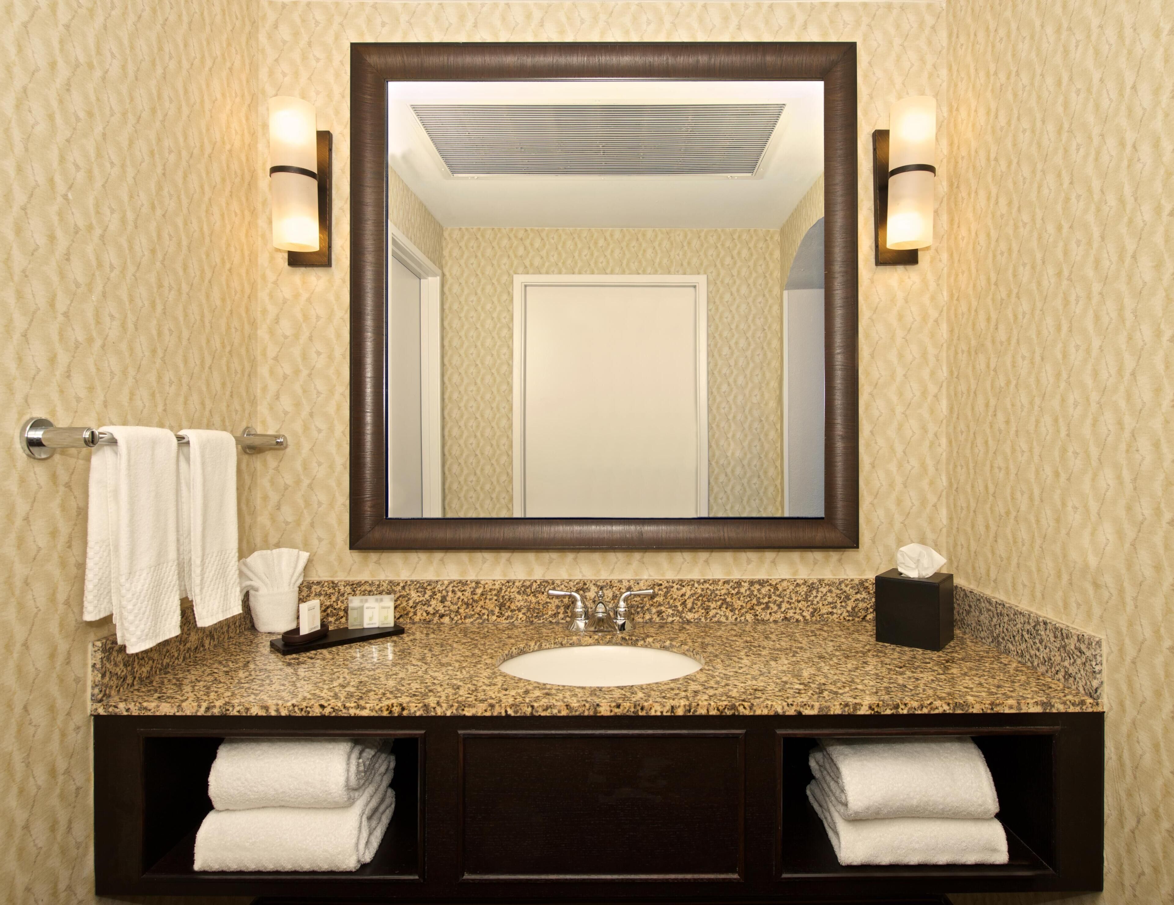 A bathroom with a granite countertop, a white sink, a dark wooden vanity, a large mirror, and two wall-mounted light fixtures.