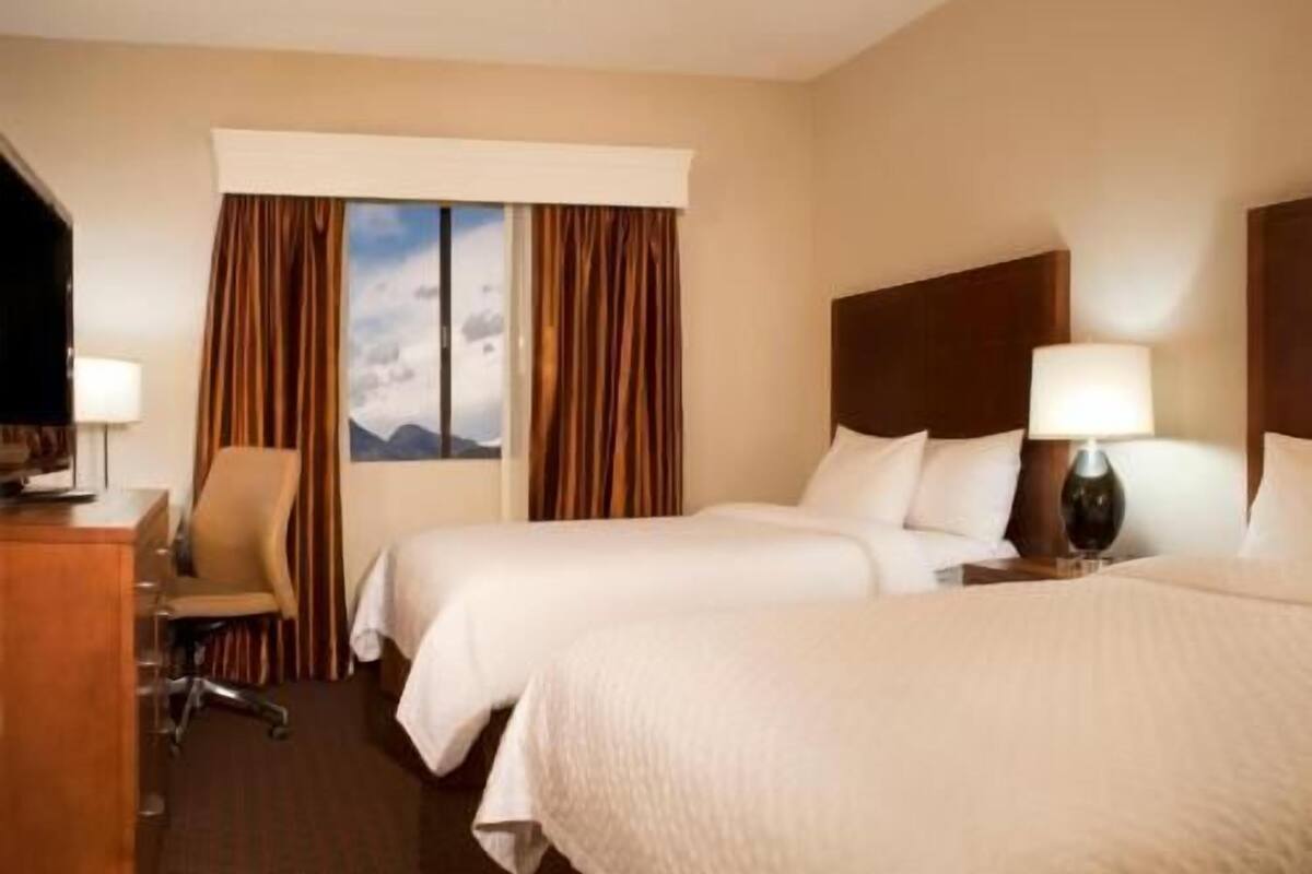 Ein Hotelzimmer mit zwei Betten, einem Schreibtisch, einem Stuhl und einem fenster mit Vorhängen.