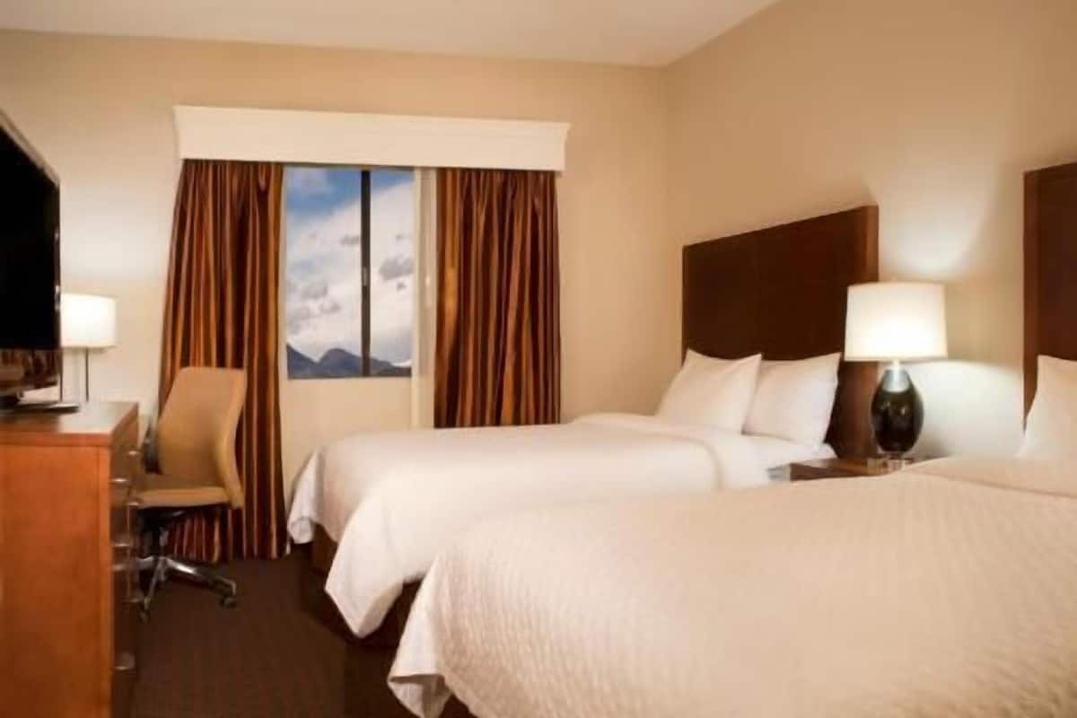 Habitación de hotel con dos camas, un escritorio, una silla y una ventana con cortinas.