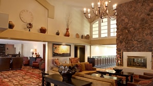 A spacious lobby with a high ceiling, a chandelier, a fireplace, and a variety of seating arrangements.