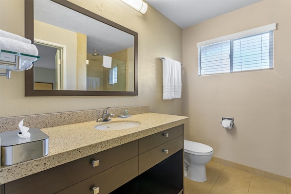 A bathroom with a double sink, a large mirror, a toilet, and a window with blinds.