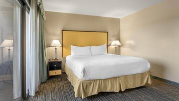 Quarto de hotel com uma cama grande, duas luminárias de cabeceira, uma mesinha de cabeceira e vista através de uma porta de vidro.