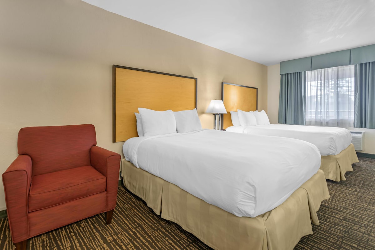 A hotel room with two beds, a red armchair, and a large window with curtains.