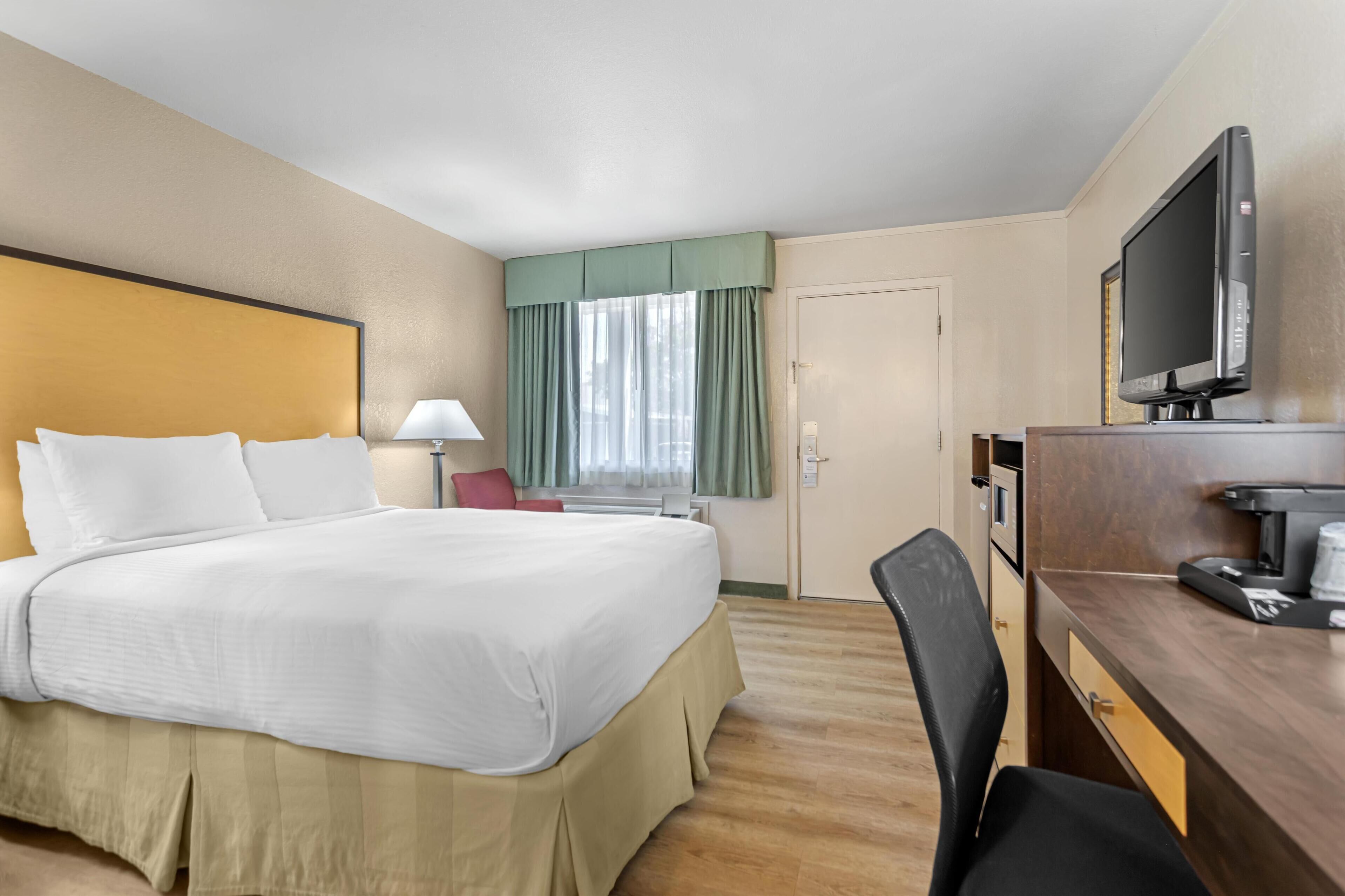 Une chambre d’hôtel avec un grand lit, un bureau avec un ordinateur, une télévision et une fenêtre avec des rideaux.