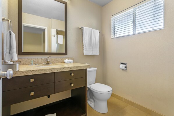 Une salle de bain équipée d’un lavabo, d’un miroir, d’un porte-serviettes, de toilettes et d’une fenêtre avec des stores.