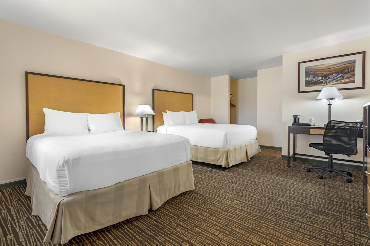 A hotel room with two beds, a desk, a chair, and a lamp.