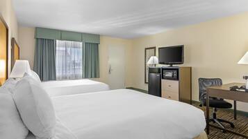 A hotel room with two beds, a desk, a television, and a refrigerator.