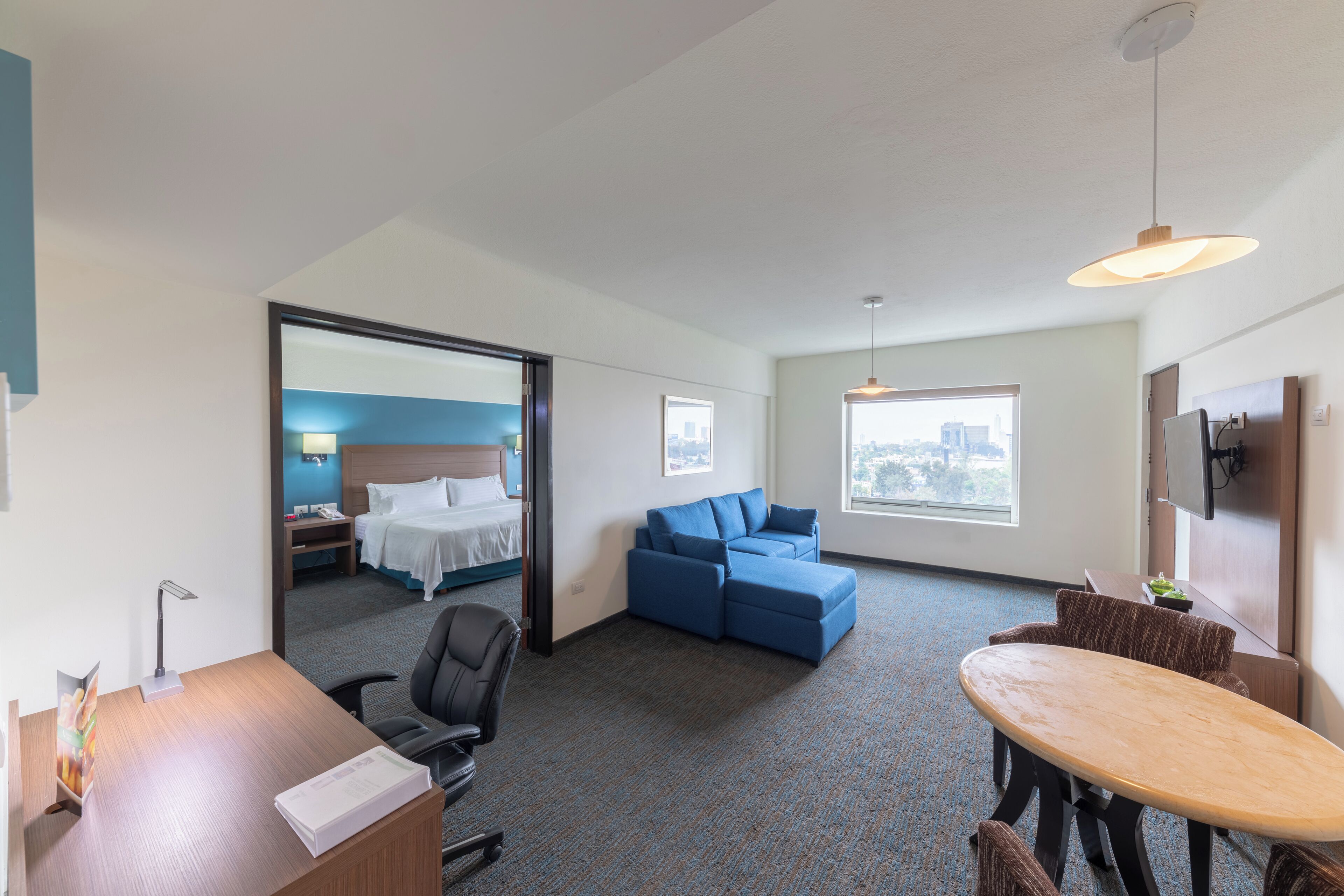 A hotel room with a bed, a sofa, a desk, and a dining area.