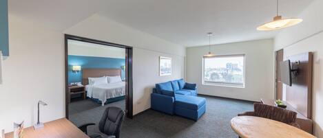 A hotel room with a bed, a sofa, a desk, and a dining area.